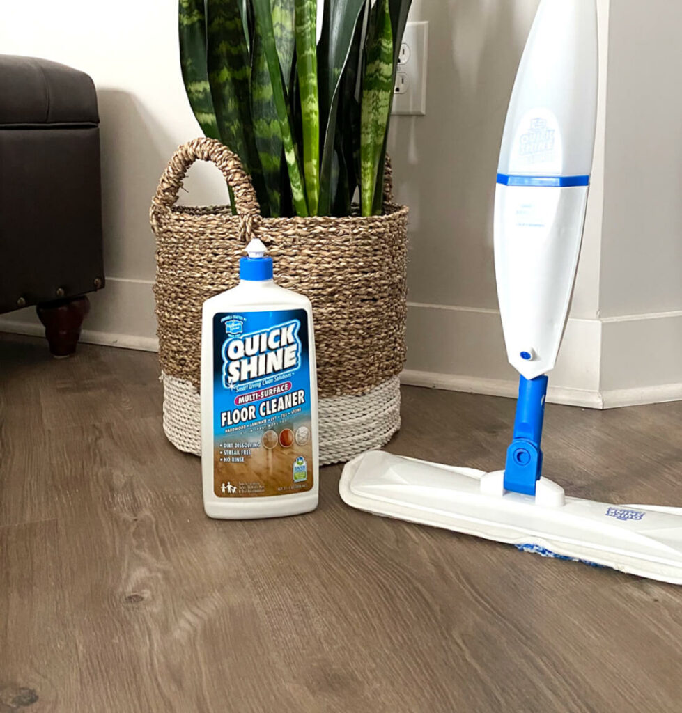 Quick Shine® Floor Cleaner and Multi-Surface Spray Mop sitting next to natural wood woven basket containing a snake plant