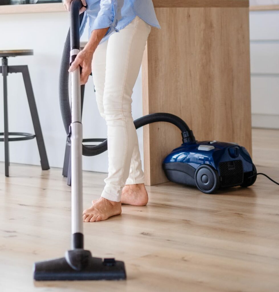 Barefoot woman in blue shirt and white pants dry vacuuming floor