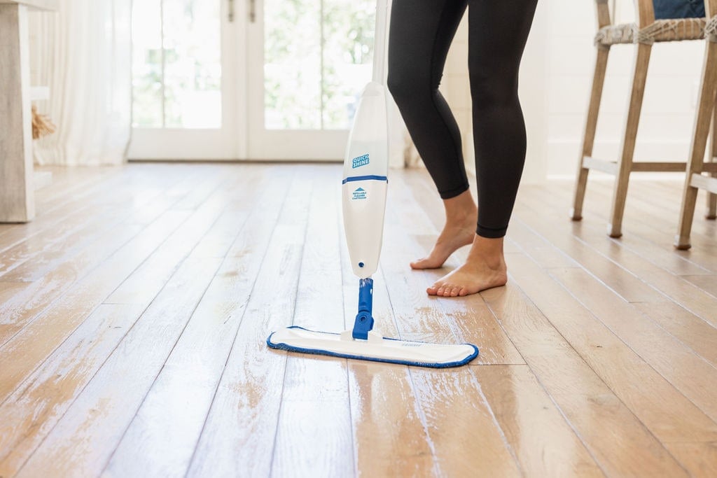 business end of quick shine spray mop on hardwood floor and female legs in background