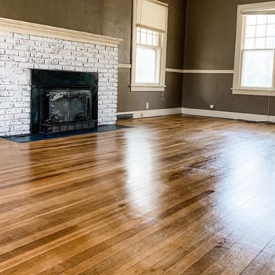 Family room with two windows, wood flooring, a fireplace with a white-washed brick surround and dark brown painted walls